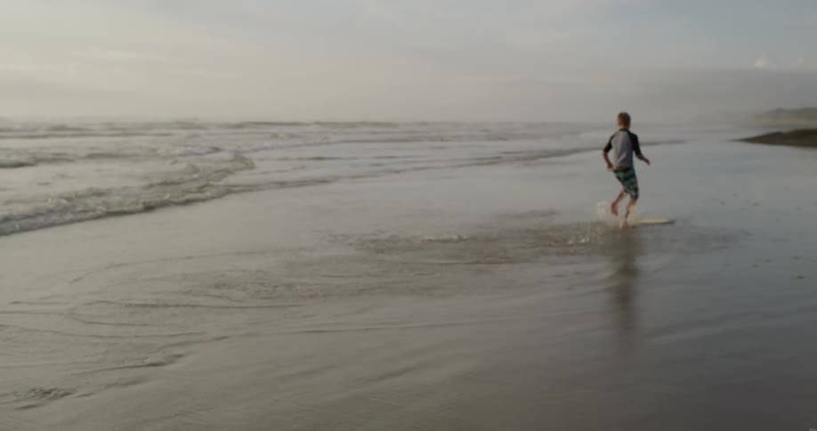 Boy throws skimboard into shallow water and then hops on it