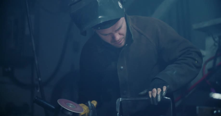 A metalworker uses a grinder to smooth a piece of metal
