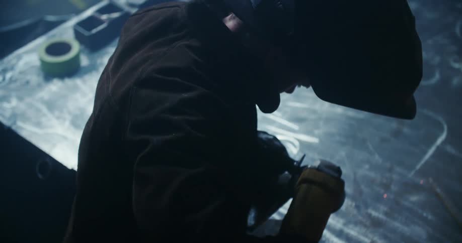 A man with a welding helmet using an electric grinder