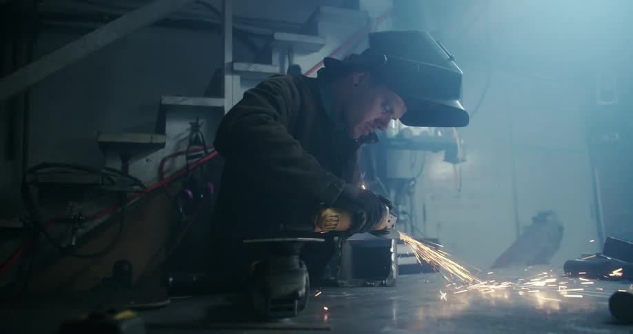 A man uses a hand saw to shave the edge of a piece of metal