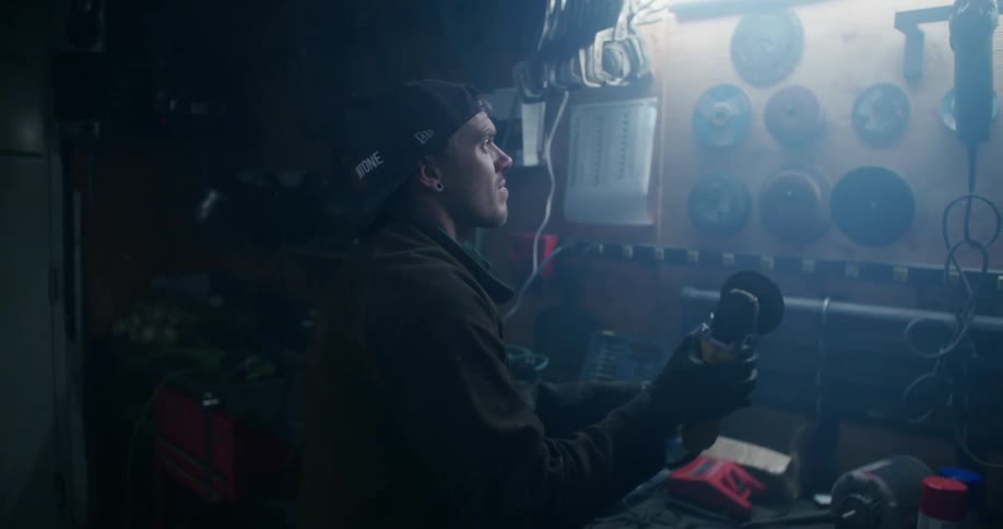 A man hanging up an electric grinder in a toolshed