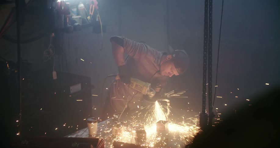 Man grinds metal box with a power tool in darkened workshop