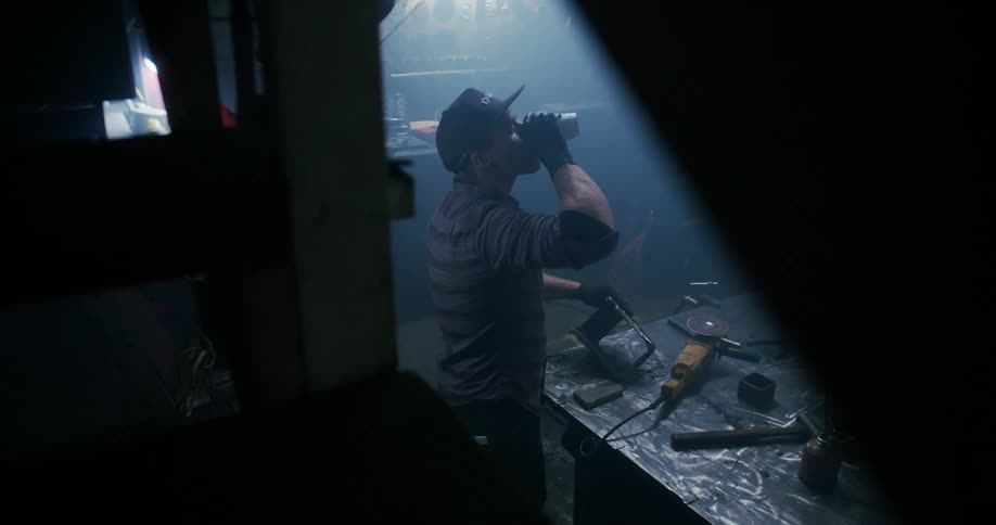 Man takes a drink while standing at a work bench