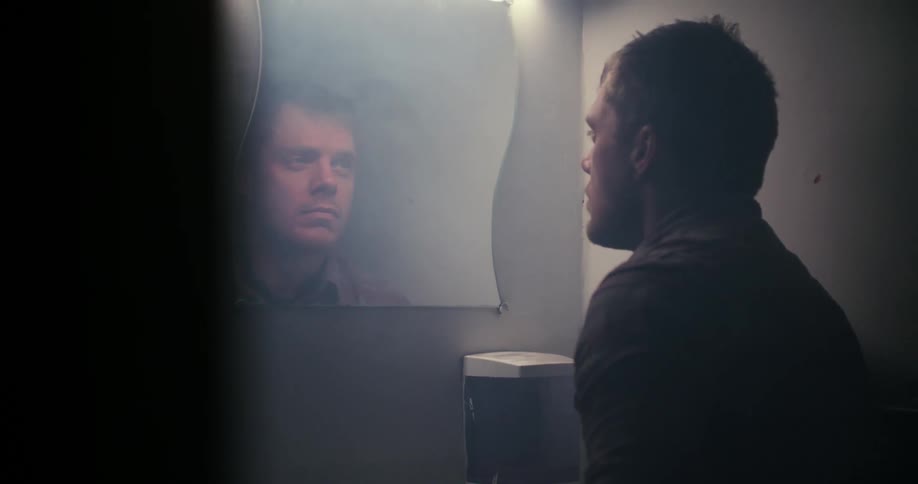 Man dries his hair with the towel and looks in the mirror in the bathroom