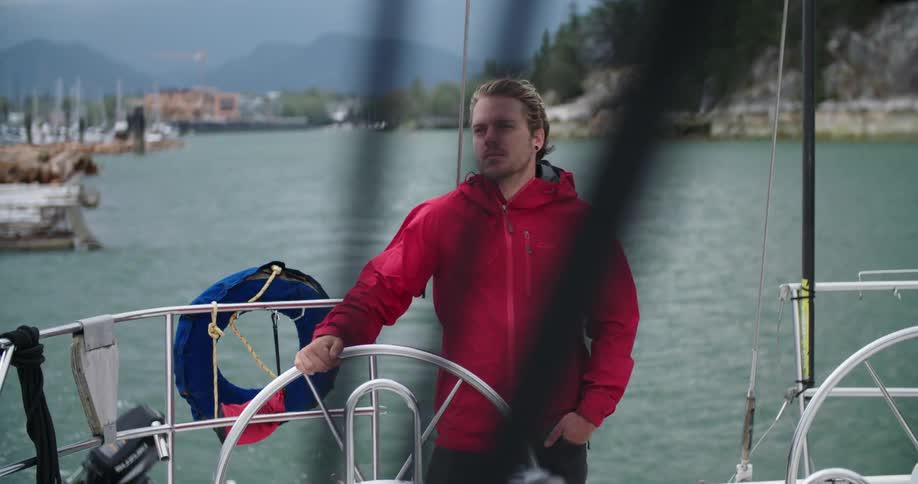 A man with a red jacket holding on to a steering wheel on a yacht