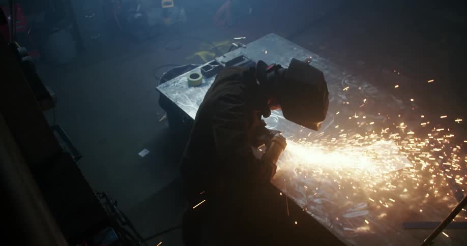 A welder creates a shower of sparks using a tool on a piece of metal