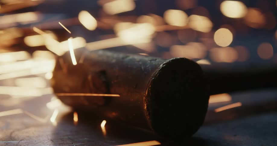 Metal hammer resting on anvil under shower of sparks
