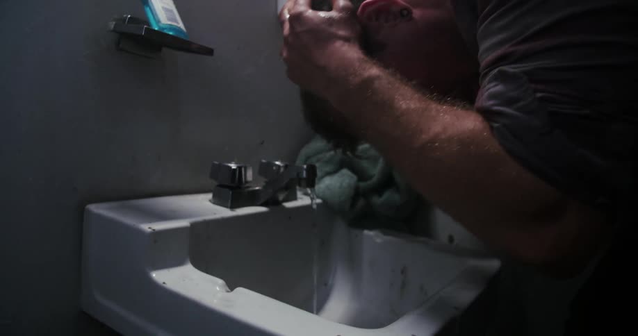 A man washes his face in a bathroom sink