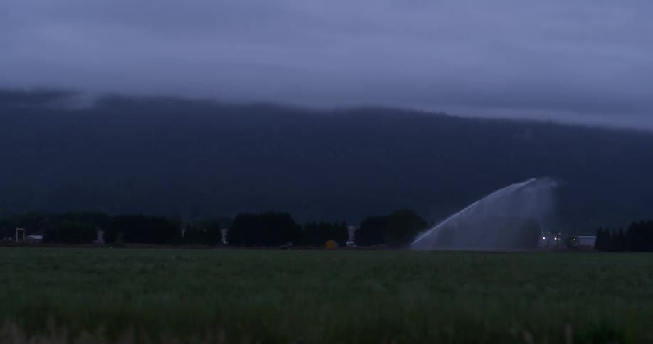 A very strong sprinkler is watering a field on a cloudy day
