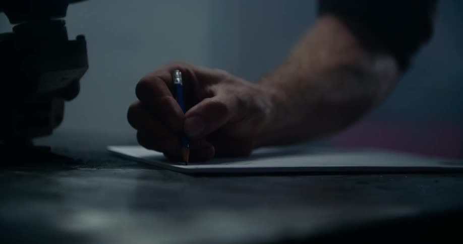 A man leaning over a workbench draws on paper with a pencil