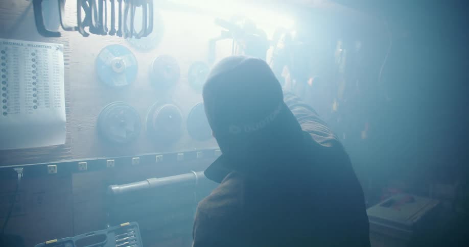 A man hangs a power tool on the wall of a garage
