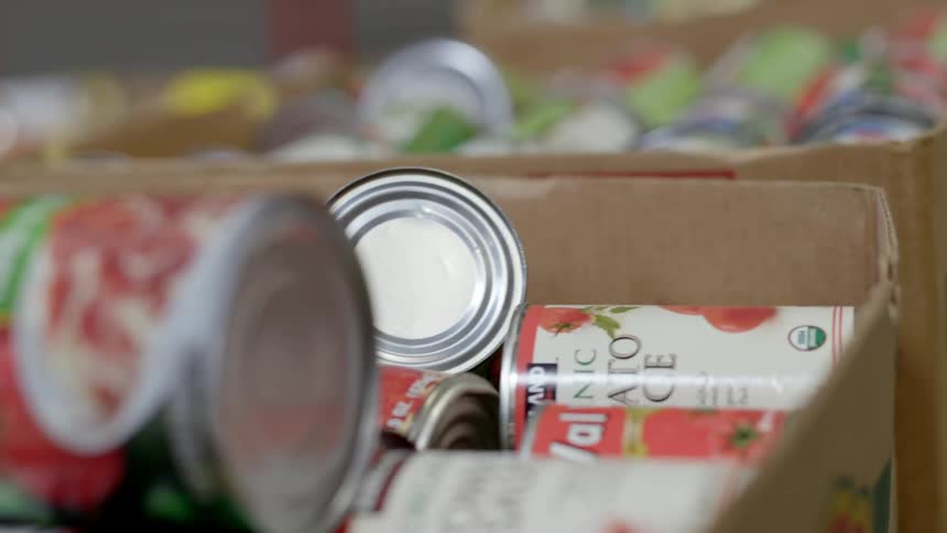 A person hand taking a can of tomato sauce out of a cardboard box