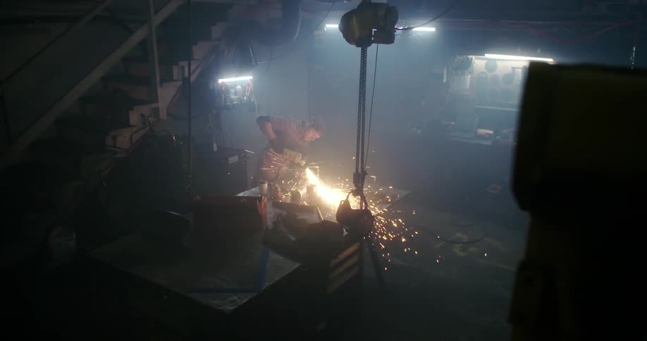 A person grinds metal in a hazy work area