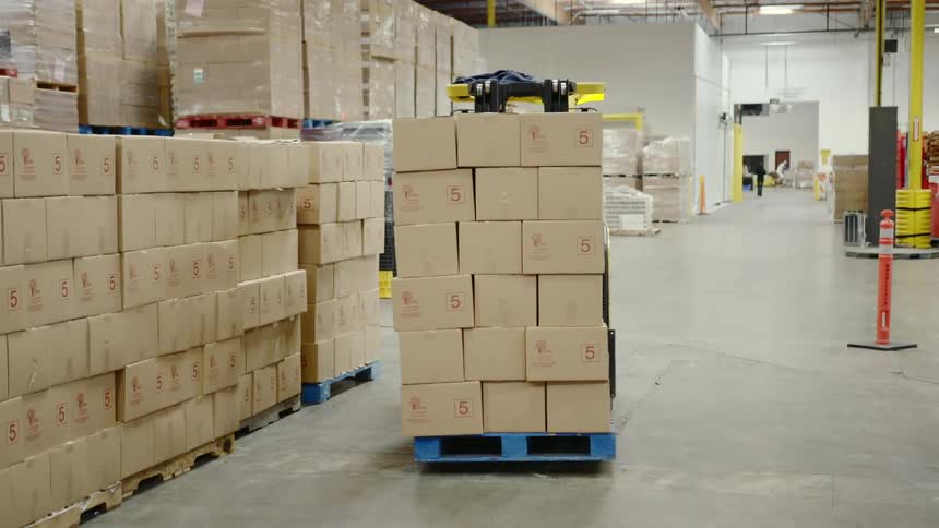 A person is working in a factory and moving boxes with a machine