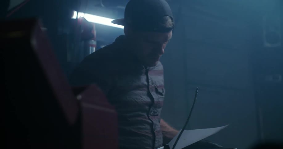 A man in a garage looking at a piece of paper and holding a metal object
