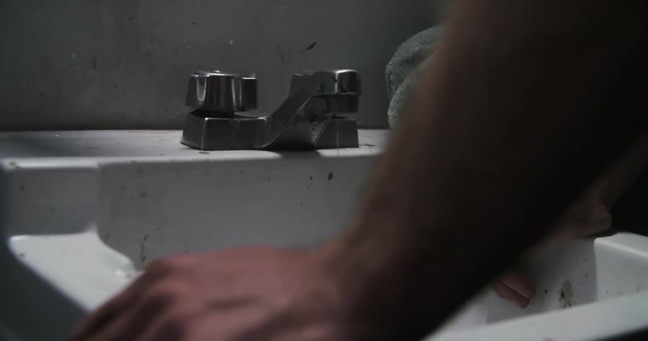 A mans hands hold onto a white bathroom sink as water drips from the faucet