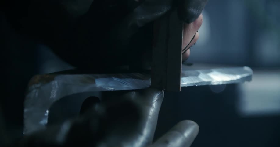 A man uses a blade to smooth a piece of metal