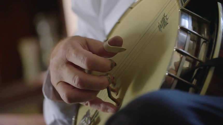 A man wearing metal finger picks and a thumb pick while playing the banjo