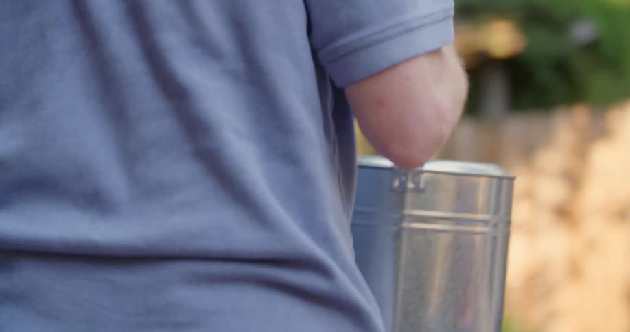 Person carrying watering can outside to water plants