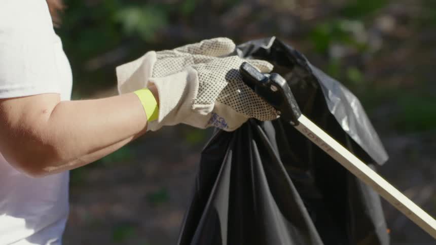 A woman walks along carrying a garbage bag as she cleans up outside