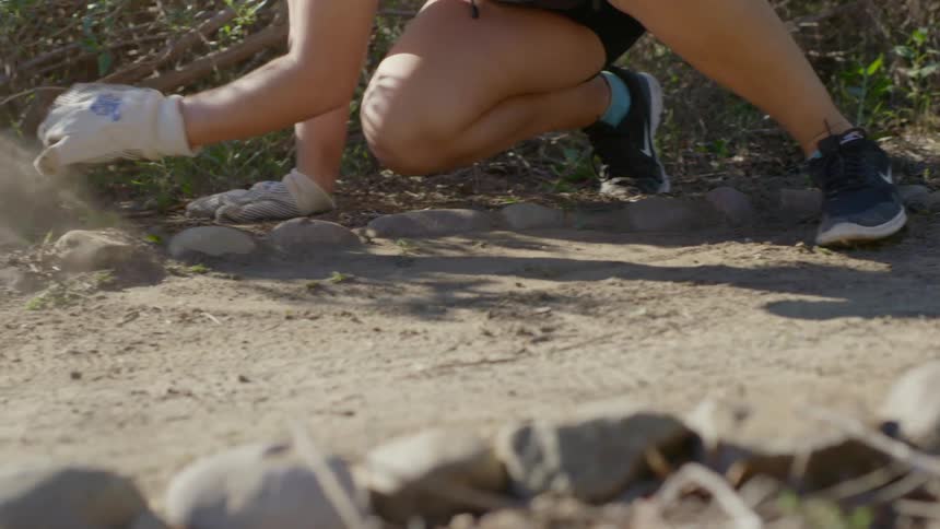 Woman in gardening gloves moves dirt through empty flower bed