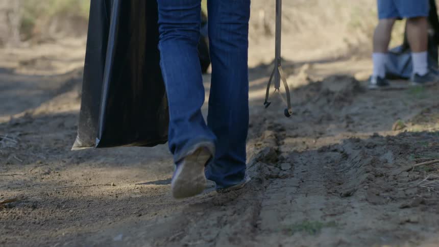 A person walks along a road with a trash bag and trash pickup tool