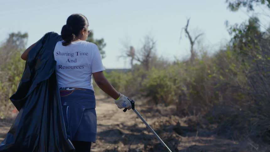 Woman carrying a black garbage bag on her back collects garbage