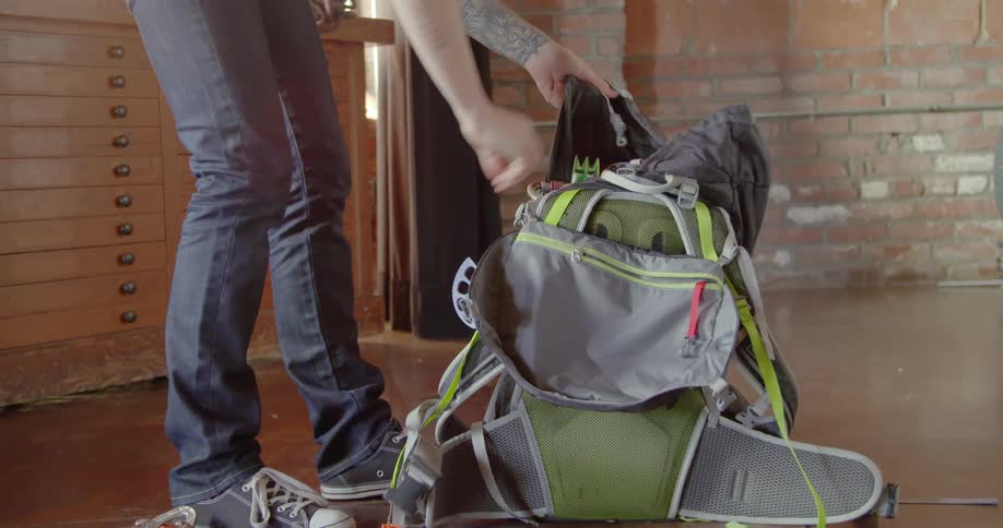 A woman picks up her backpack and puts the items back in it and shakes to settle the contents