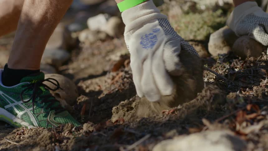 Man in gardening gloves clear rocks from yard