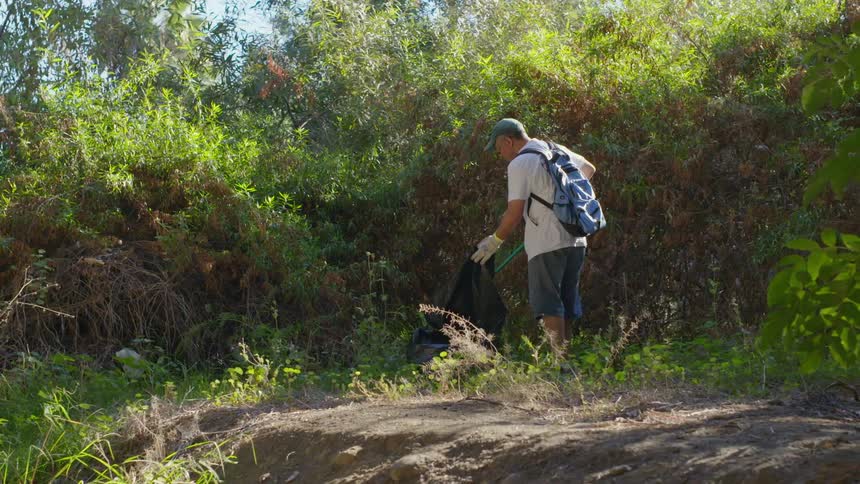 A man using a tool to collect garbage in the wilderness
