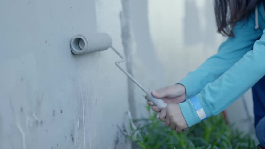 Woman painting an outdoor wall with a paint roller