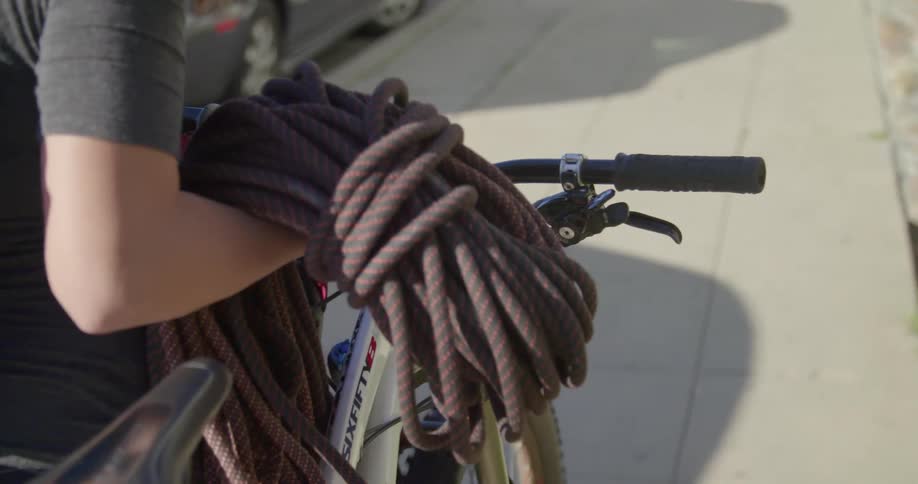 A woman carries a large bundle of rope while pushing a bike down a sidewalk