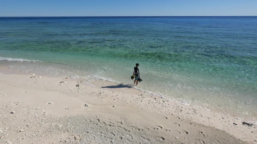 A snorkeler walks along a sandy beach