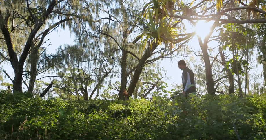 A man walks through an overgrown area holding flippers