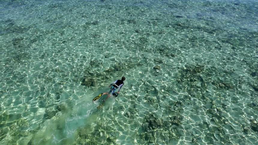 A man snorkeling in very clear water as he pulls a camera alongside