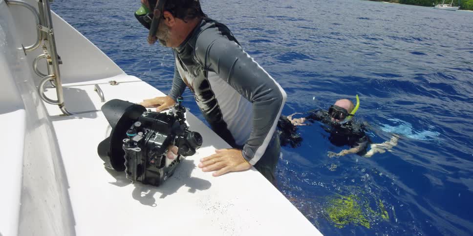 Two divers swim over to a boat and place the camera on it before climbing up