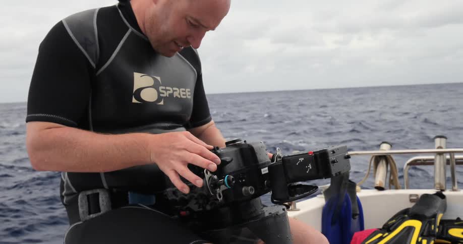 Man sitting on a boat pressing buttons on underwater camera
