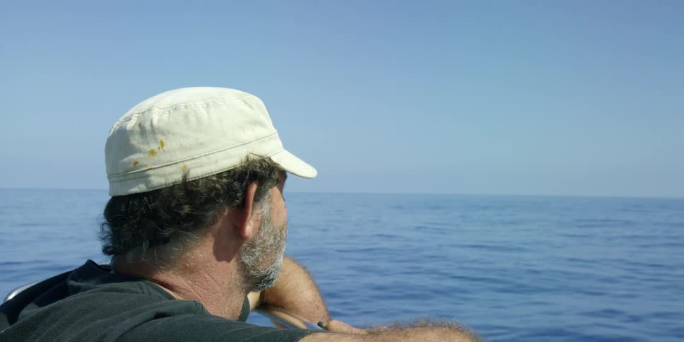 A medium shot of a man leaning on the railing of a boat and looking around at the open waters of the ocean