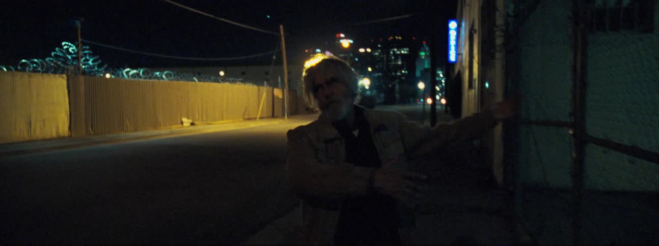 A drunk older man bounces off a city building at night as he attempts to walk down an alley