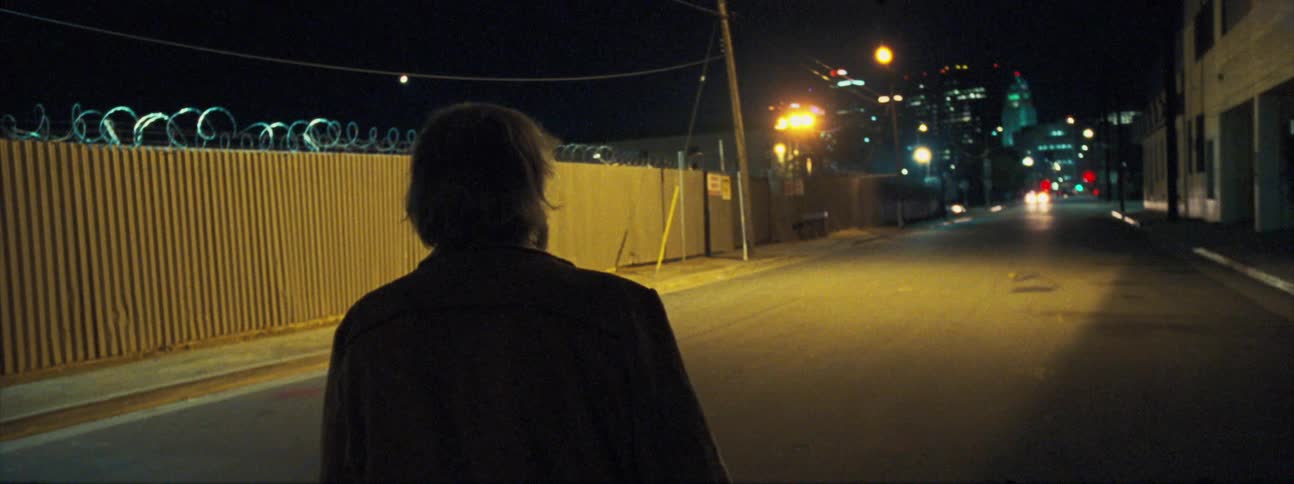 A befuddled old man standing in a city street looking around at night