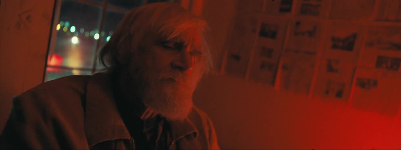 Elderly man closes eyes and sways near windows in red lit room