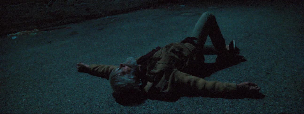 An elderly man breaks down and waves his arms while laying on the ground outside