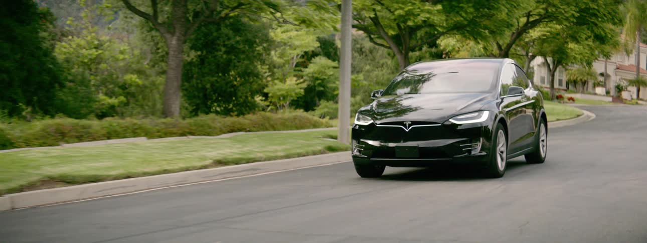 A black car driving on the road with a house in the background