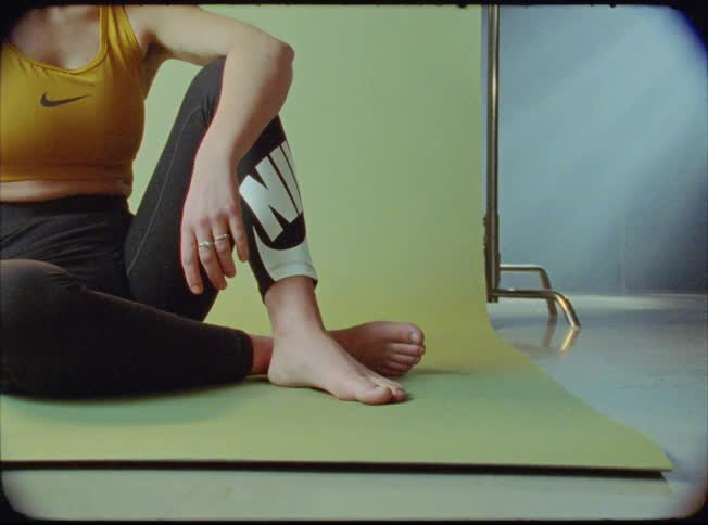 A woman in workout gear sits on a mat tapping her foot