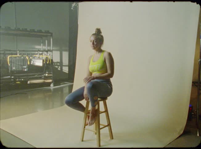 A young woman coming to sit on a stool in front of a photography backdrop