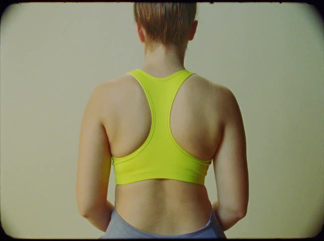 A woman sits on a stool wearing a sports bra