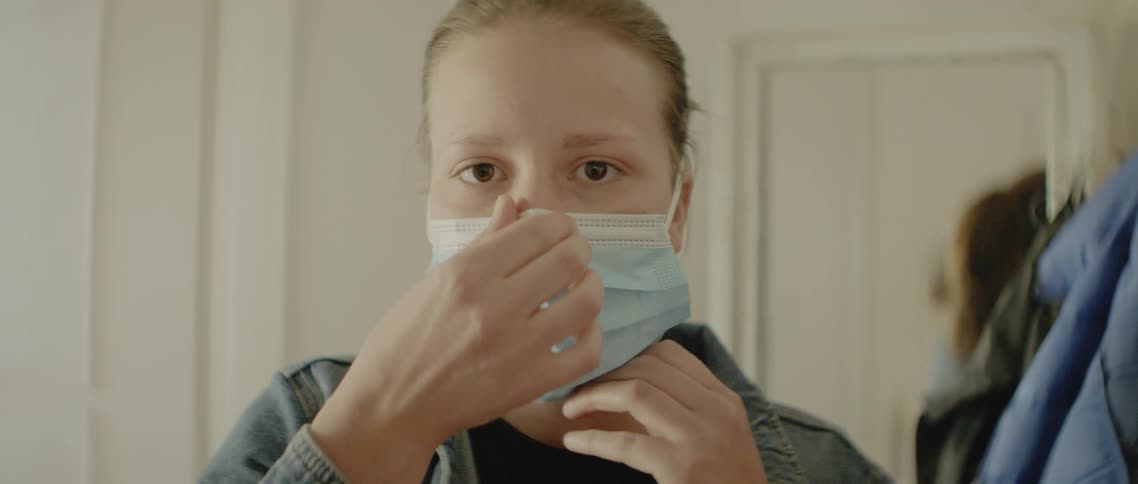 Woman looking in the mirror wears a face mask at home