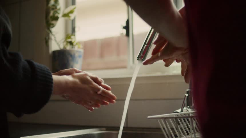 A man and woman wash their hands at their kitchen sink