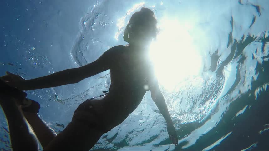 Sun shines from overhead onto women wearing a bikini and snorkeling