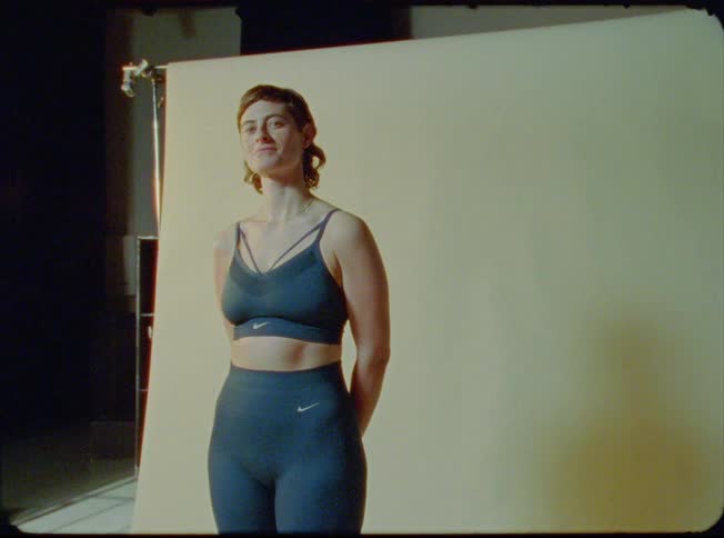 A woman stands in front of a back drop wearing athletic gear